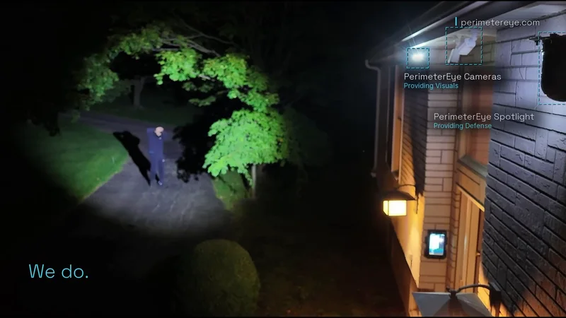 The searchlight catching a person on the dark driveway as they raise their hands against the light, with the PerimeterEye cameras and searchlight labeled